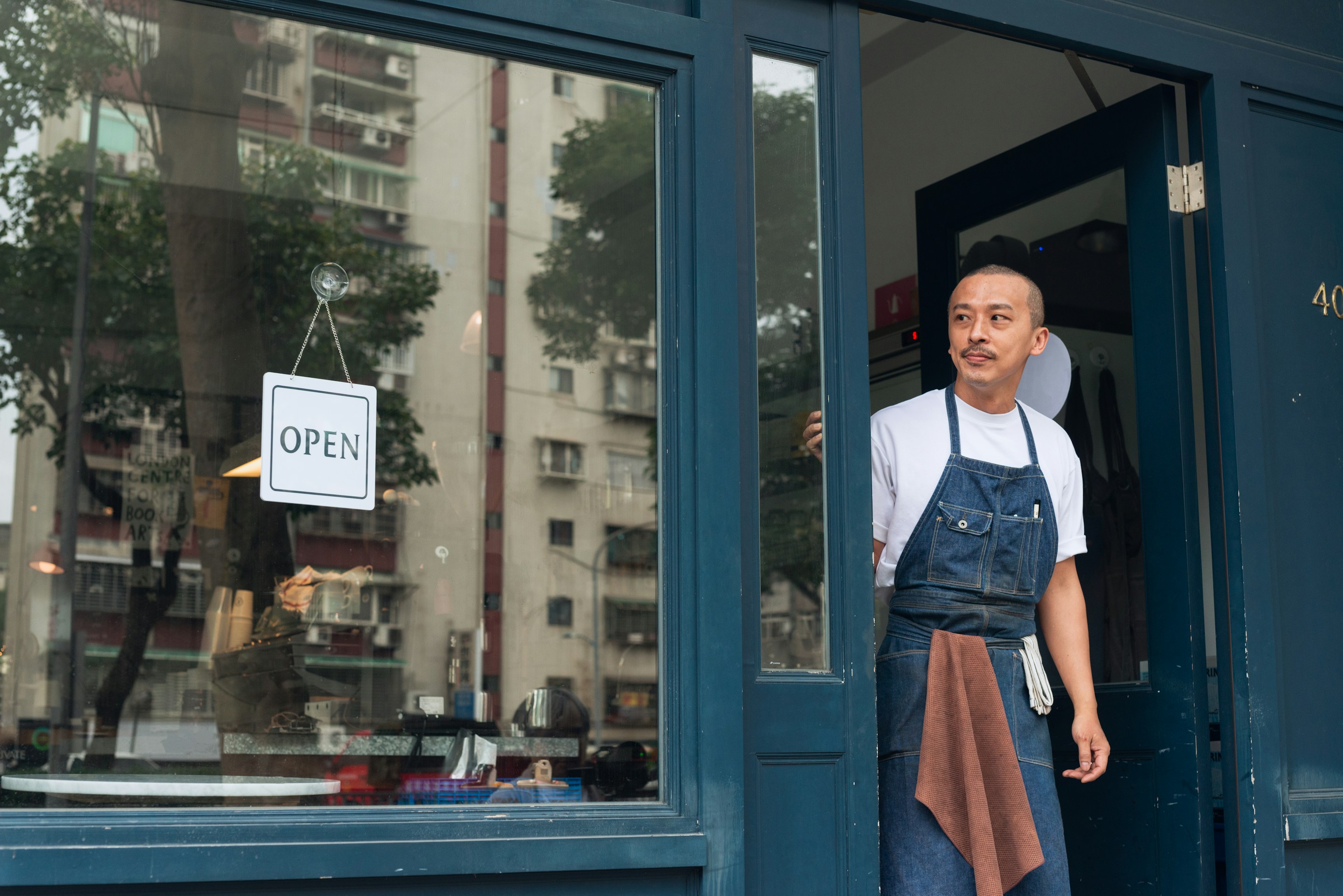 A small-business owner standing in the doorway beside an OPEN sign